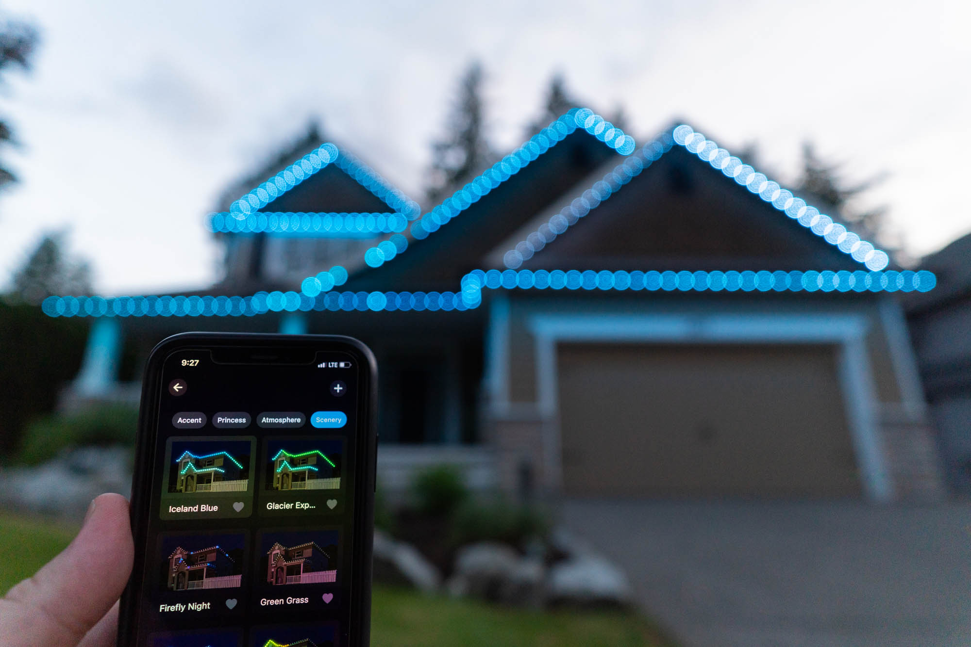 Hand holding the Chromaglow app with a home lit in ice blue behind